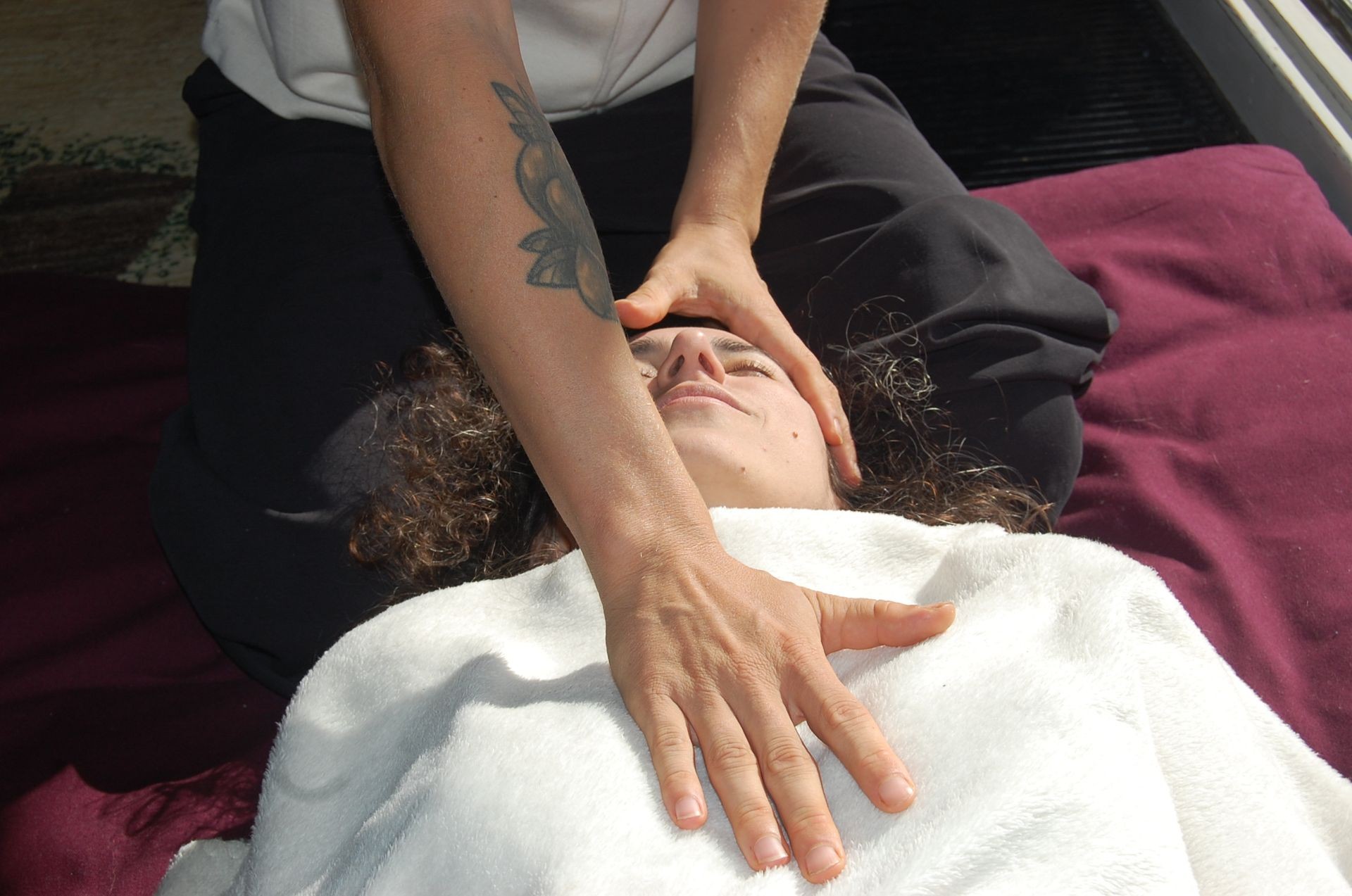 Person receiving a head and chest massage on a burgundy mat, covered with a white towel.