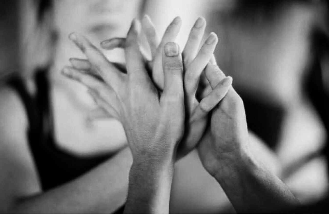 Close-up black and white photo of two people's hands touching gently with fingers intertwined.